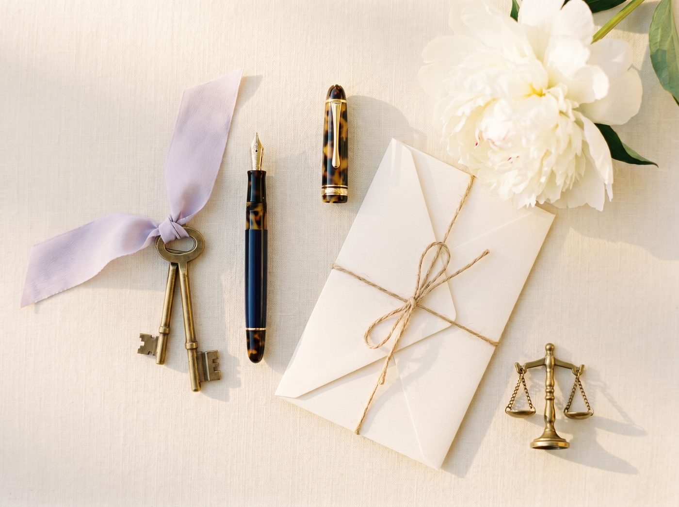Closing-day flat-lay with brass keys, fountain pen, and white peony